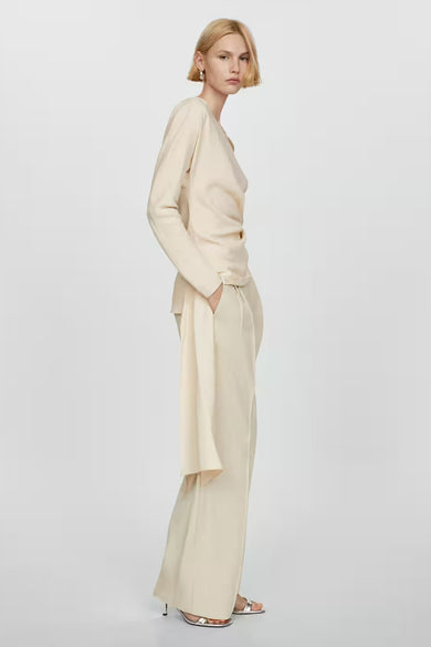 Blouse beige de MANGO avec manches longues, drapée sur le devant, portée avec un pantalon ample.
