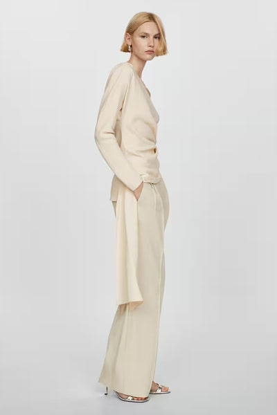 Blouse beige de MANGO avec manches longues, drapée sur le devant, portée avec un pantalon ample.
