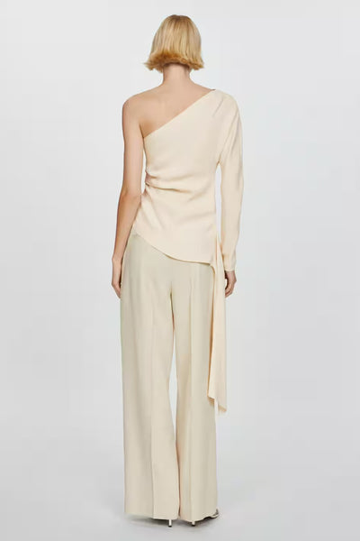 Blouse beige asymétrique de MANGO, avec une manche longue et une coupe fluide tombant sur un pantalon large.
