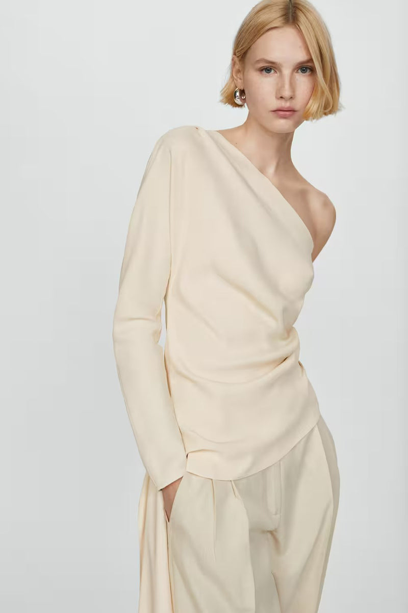 Blouse beige à une épaule de MANGO, avec une manche longue et tombé drapé, portée avec un pantalon assorti.