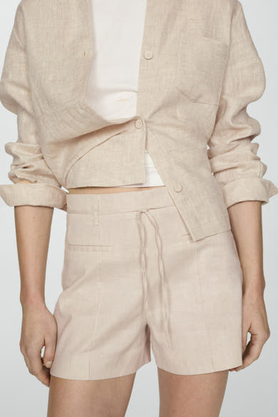 Korte beige short van MANGO, gedragen met een witte tanktop, van achteren gezien.