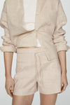 Korte beige short van MANGO, gedragen met een witte tanktop, van achteren gezien.