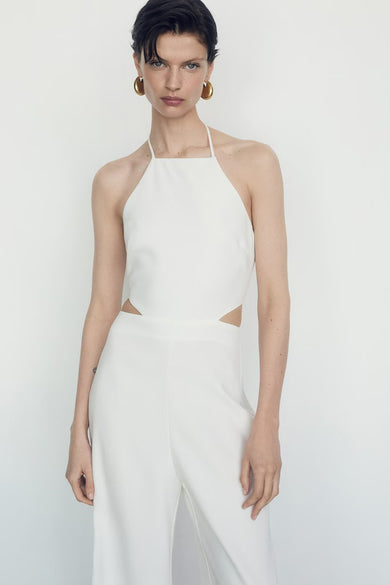 Combinaison beige de MANGO, avec coupe au niveau de la taille et dos nu, porté avec des boucles d'oreilles dorées.
