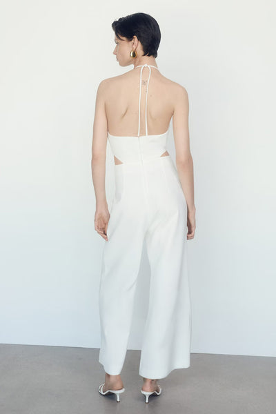 Combinaison beige de MANGO avec dos nu et découpes latérales, portée avec des mules blanches.