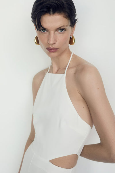 Combinaison beige de MANGO avec dos nu, coupe à la taille et boucles d'oreilles dorées.