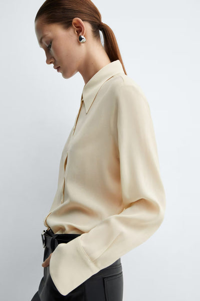 Chemisier à manches longues jaune de MANGO, avec col classique et fermeture boutonnée, porté avec un pantalon noir.
