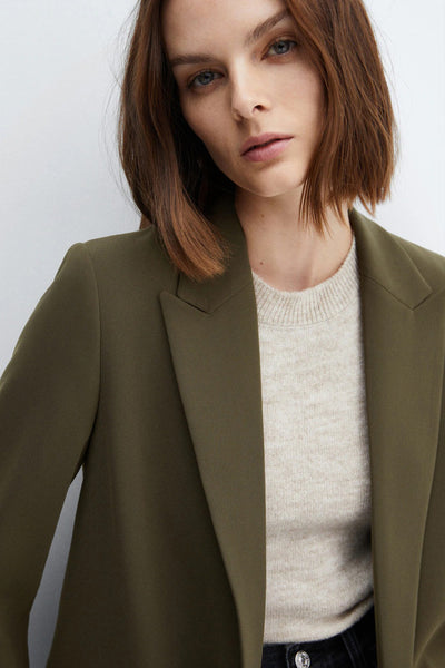 Blazer vert de MANGO, porté sur un pull en maille neutre, devant un fond blanc uni.