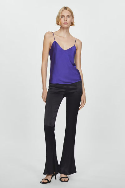 Top bleu à fines bretelles de MANGO, porté avec un pantalon noir évasé et des sandales à talons.