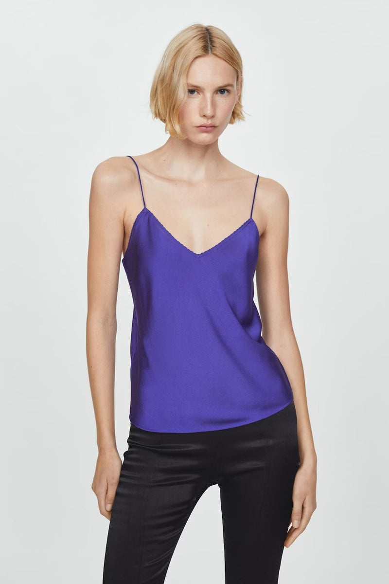 Top bleu à fines bretelles de MANGO, porté avec un pantalon noir brillant.
