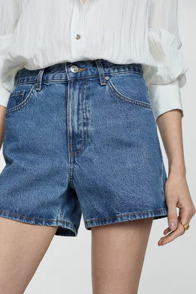 Short en denim bleu de MANGO, avec une boutonnière apparente, porté avec une chemise blanche.