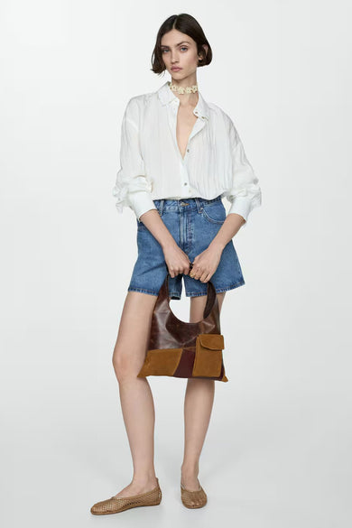 Short en denim de MANGO, porté avec une chemise blanche et un sac patchwork.