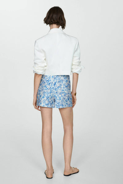 Short bleu à motif floral de MANGO, porté avec un blazer blanc court.
