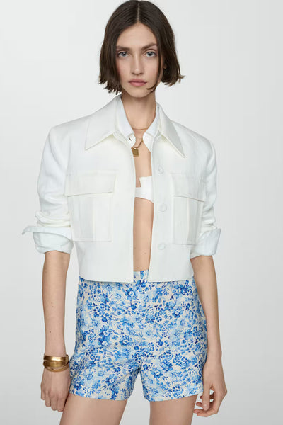 Short bleu à fleurs de MANGO, porté avec une veste blanche et un bracelet doré.
