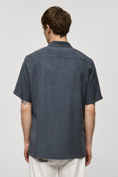 Chemise bleu à manches courtes de MANGO, vue de dos, portée avec un pantalon blanc.