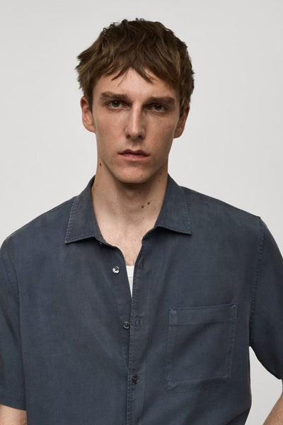 Blauw overhemd met korte mouwen van MANGO, met borstzak en klassieke kraag, gedragen over een wit T-shirt.