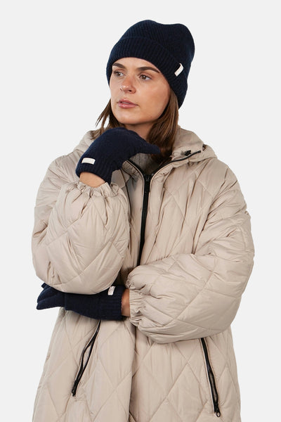 Gants bleus en maille de BARTS, portés avec un bonnet bleu assorti et un manteau matelassé beige.