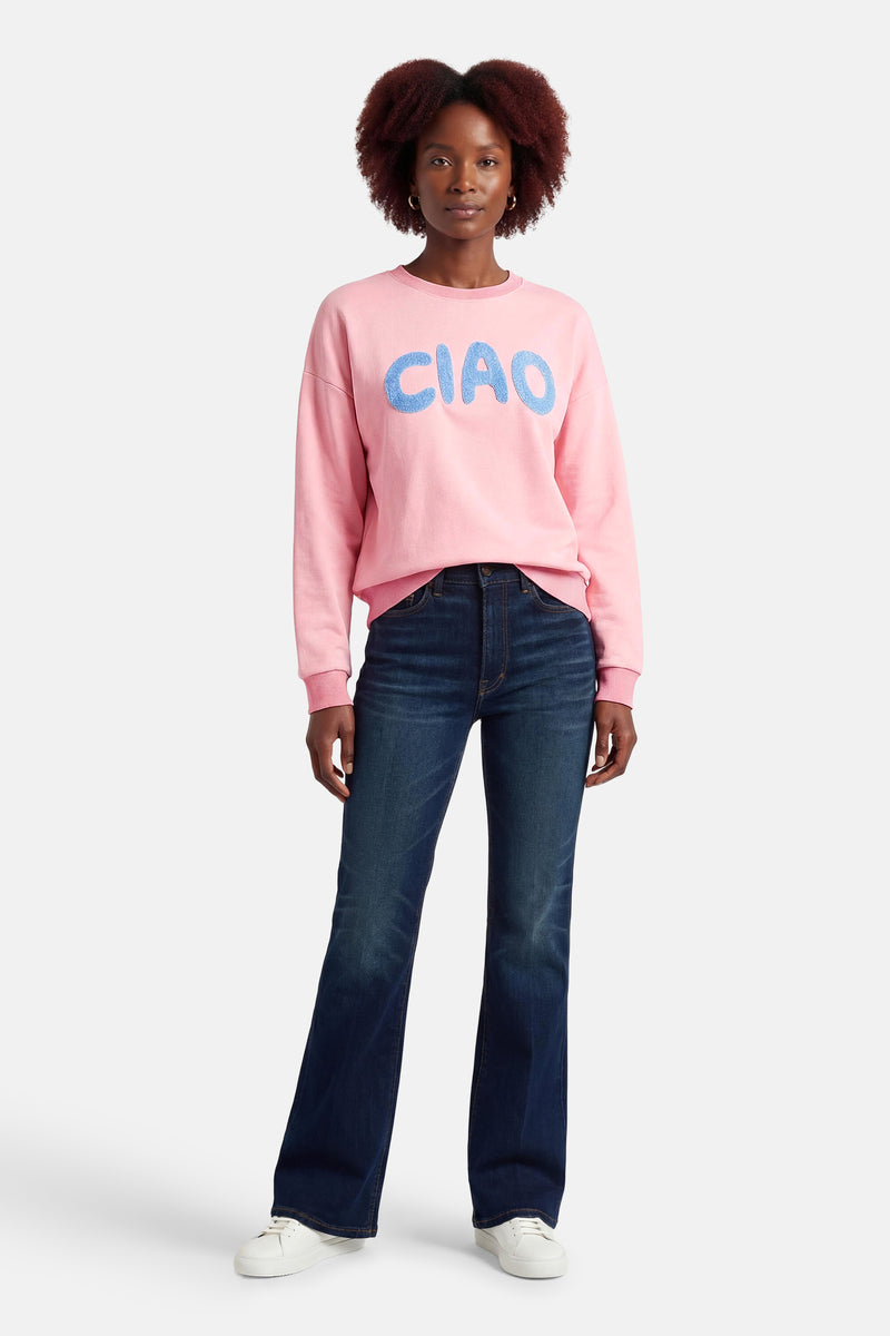 Terra di Siena sweatshirt met lichtblauwe belettering, gedragen met wijde jeans en witte sneakers.