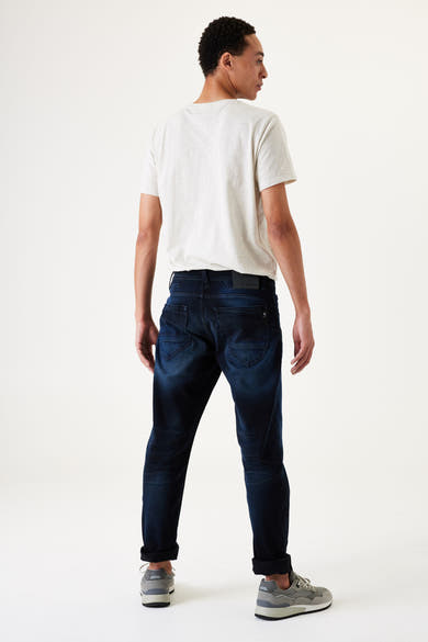 Jean slim en denim bleu foncé de GARCIA, porté avec un t-shirt couleur crème et des baskets grises, vue de dos.
