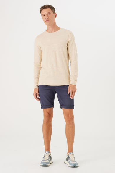 Short en denim bleu de GARCIA, porté avec un t-shirt beige à manches longues et des baskets.
