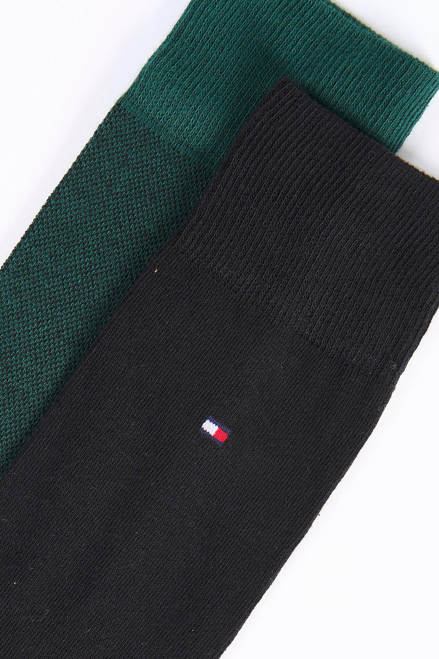 Gros plan sur des chaussettes courtes TOMMY JEANS noires et vert foncé, avec un petit drapeau tricolore brodé.