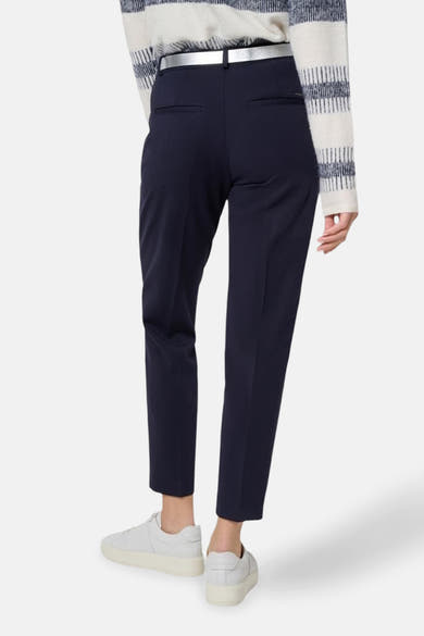 Pantalon de costume bleu de BRAX, avec ceinture argentée et poches arrière discrètes, porté avec des baskets blanches.
