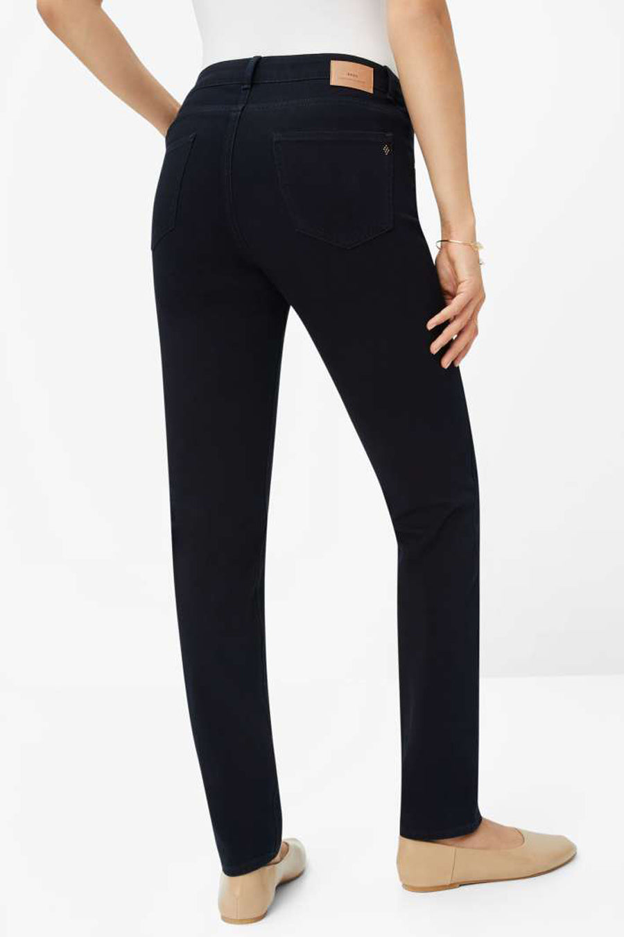 Jean slim en denim bleu noir par BRAX, avec poches arrière et chaussures plates beiges.
