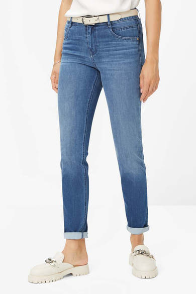 Jean slim en denim bleu moyen de BRAX, porté avec une ceinture claire et des chaussures blanches.
