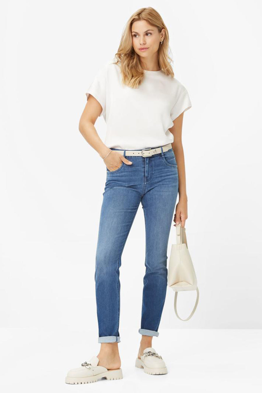 Jean slim en denim bleu moyen de BRAX, porté avec un t-shirt blanc et des mocassins couleur crème.