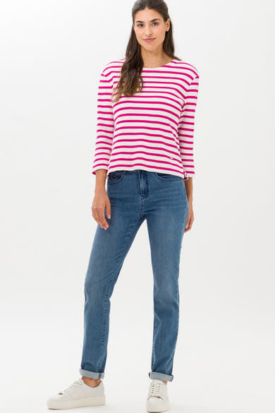 Rechte middinblauwe denim jeans van BRAX, gedragen met een rood-wit gestreept T-shirt en witte sneakers.