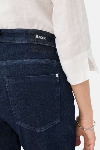 Jean large en denim bleu foncé de BRAX, avec une poche arrière et une chemise blanche en lin.