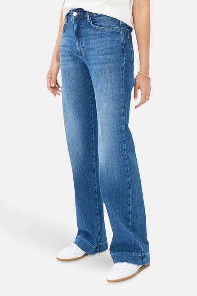 Jean large en denim bleu moyen de BRAX, porté avec des baskets blanches et un bracelet discret.
