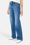 Jean large en denim bleu moyen de BRAX, porté avec des baskets blanches et un bracelet discret.
