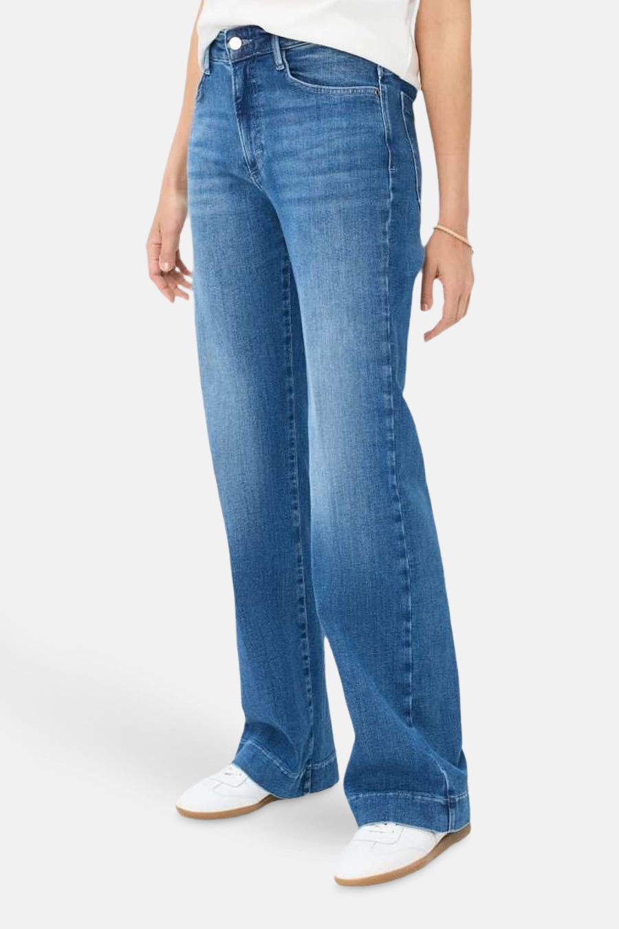 Jean large en denim bleu moyen de BRAX, porté avec des baskets blanches et un bracelet discret.
