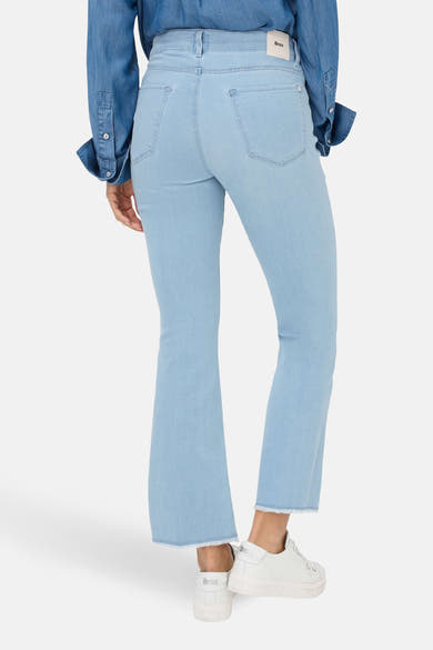 Jean slim en denim bleu clair de Brax, avec ourlet effiloché et chaussures blanches.
