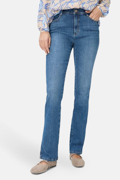 Jean bootcut en denim bleu moyen de BRAX, coupe droite, porté avec un chemisier à motifs.
