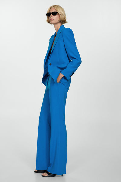 Pantalon de costume bleu par MANGO, coupe évasée, porté avec un blazer assorti et des sandales noires.