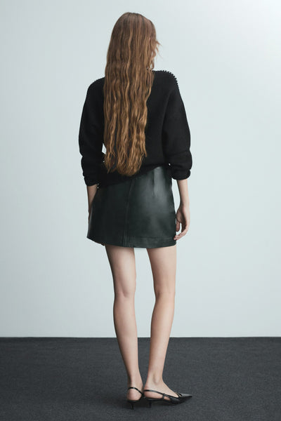 Multikleuren rondehals trui van MANGO, gedragen met een zwarte leren rok en hakken.