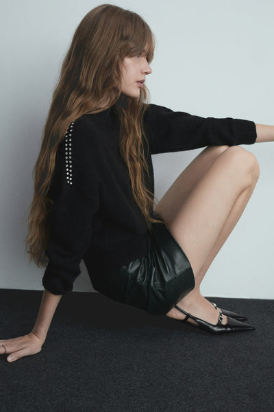 Pull à col rond multicolore de MANGO, orné de strass aux épaules, porté avec un short noir en similicuir et des escarpins noirs.
