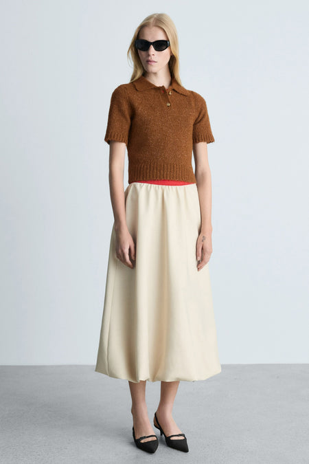 Bruine trui met ronde hals van MANGO met korte mouwen, gedragen met een beige midirok en zwarte pumps.