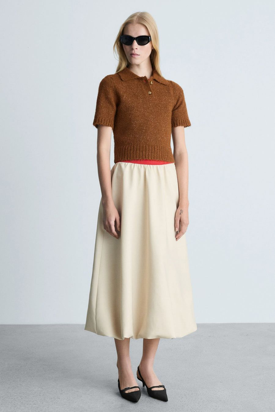 Bruine trui met ronde hals van MANGO met korte mouwen, gedragen met een beige midirok en zwarte pumps.