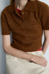 Bruine trui met ronde hals van MANGO, met glanzende textuur, gedragen over een rood T-shirt en een lichte broek.