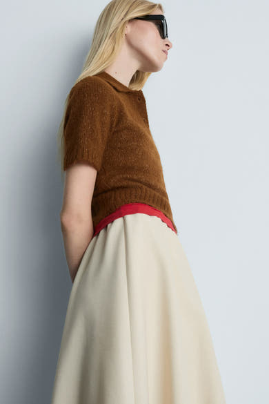 Bruine trui met ronde hals van MANGO, met korte mouwen en rode bies, gedragen met een beige rok.