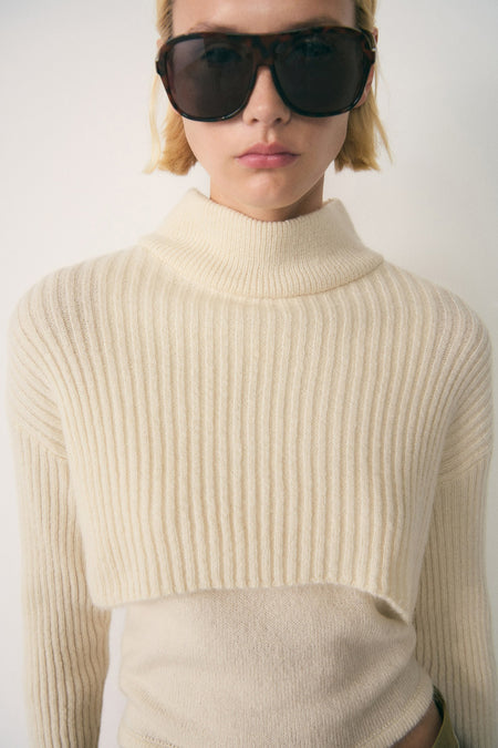 Witte coltrui van MANGO, gedragen met een andere beige trui eronder en een bruine zonnebril.