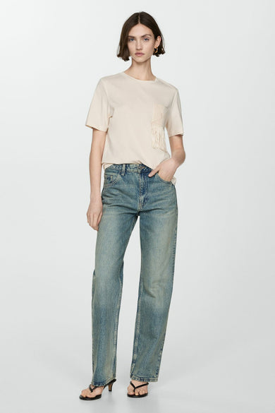 T-shirt beige à manches courtes de MANGO, avec poche ornée de franges, porté avec un jean bleu.