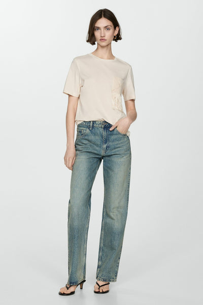 T-shirt beige à manches courtes de MANGO, avec poche ornée de franges, porté avec un jean bleu.