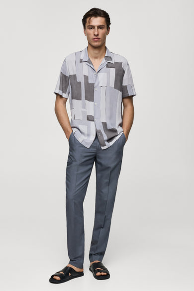 Chemise à manches longues grise de MANGO avec motif géométrique, portée avec un pantalon bleu et des sandales noires.