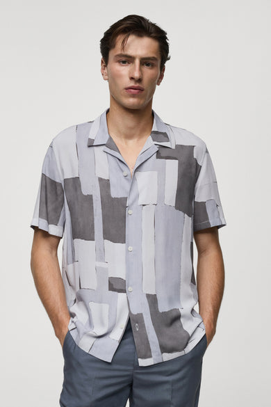 Chemise grise à manches courtes de MANGO, à motif géométrique et coupe décontractée, portée avec un pantalon bleu ardoise.