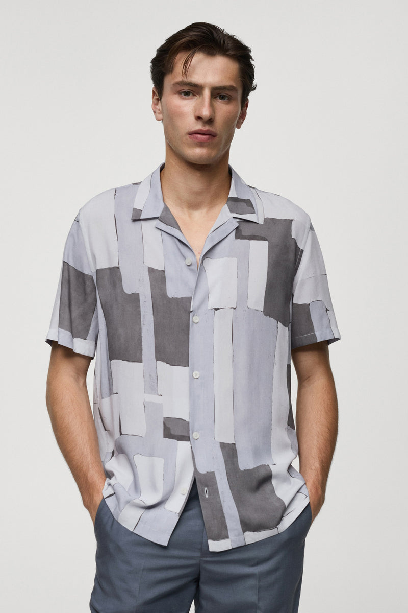 Chemise grise à manches courtes de MANGO, à motif géométrique et coupe décontractée, portée avec un pantalon bleu ardoise.
