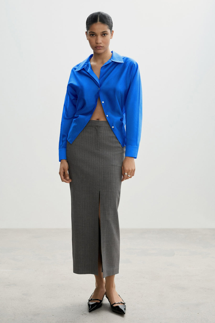Blauwe blouse met lange mouwen van MANGO, open gedragen met een gestreepte kokerrok en zwarte pumps.