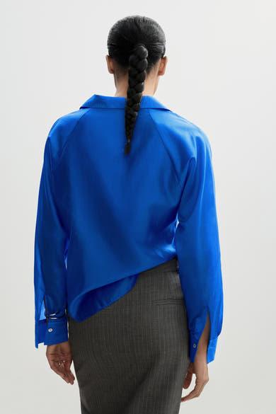 Chemise bleue à manches longues de MANGO, avec un style ample et un détail de tresse dans les cheveux.
